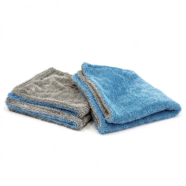Two folded microfiber towels, one gray side and one blue side, on a white background