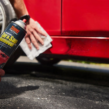 Person cleaning a red car with a can of Stoner tar and sap remover.