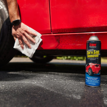 Person cleaning a red car with a cloth, next to a can of Stoner Tar & Sap Remover.