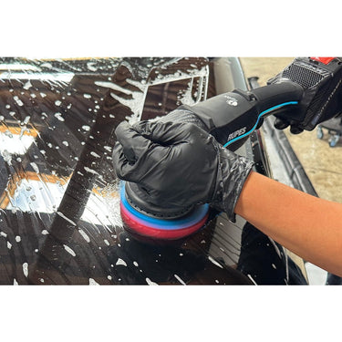A person using the black clay disc with red inner foam on polisher.